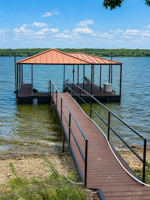 Un muelle de madera que conduce a una zona cubierta para el lanzamiento de barcos, con un banco y una mesa.