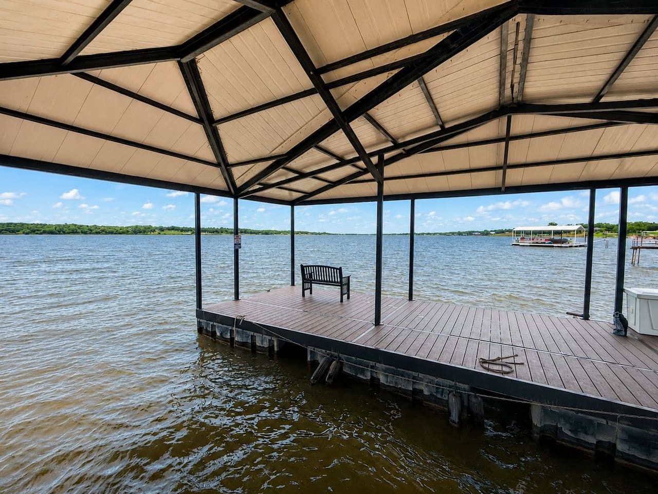A covered dock with a bench, extending over water.