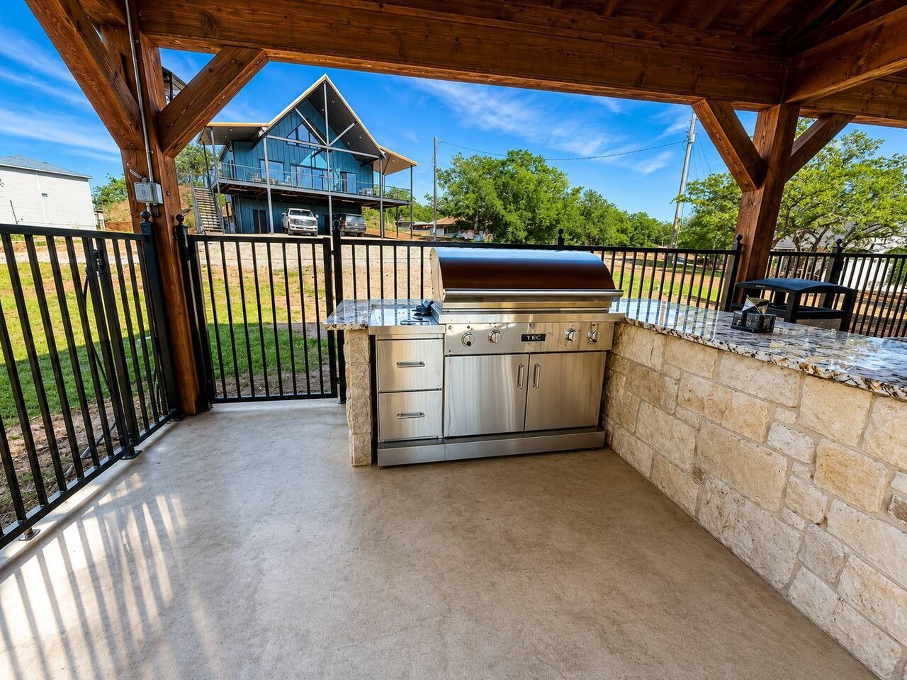 An outdoor kitchen area with a grill, stone wall, and a view of a house in the background.