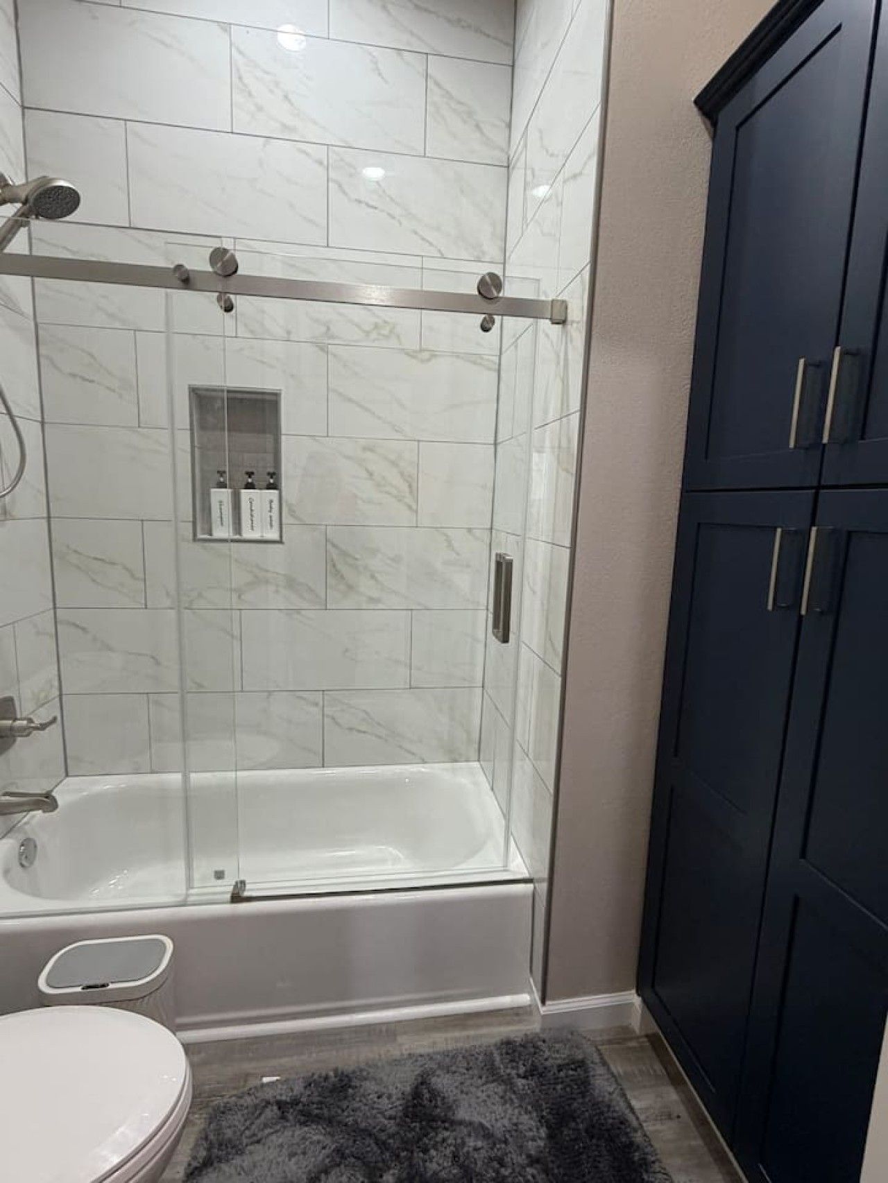 A bathroom with a glass-enclosed shower, a white bathtub, and a dark cabinet.