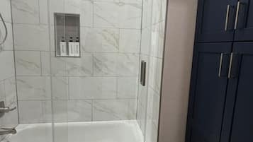 A bathroom with a glass-enclosed shower, a white bathtub, and a dark cabinet.