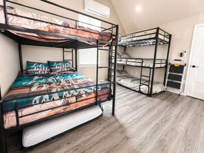 Habitación con literas, piso de madera, una puerta blanca y un equipo de aire acondicionado en la pared.
