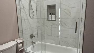 Un bany modern amb dutxa tancada amb vidre, un vàter blanc i una banyera.