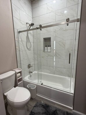 Un baño moderno con ducha envuelta en vidrio, inodoro blanco y bañera.
