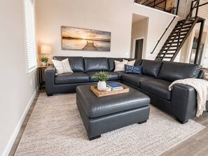 A modern living room with a sectional sofa, a coffee table, and a painting on the wall. - Waterfront Retreat | Hot Tub, Outdoor Kitchen & Private Dock (Nocona)