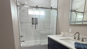 Un bagno moderno con doccia vetro, lavandino bianco con specchio e mobili scuri.