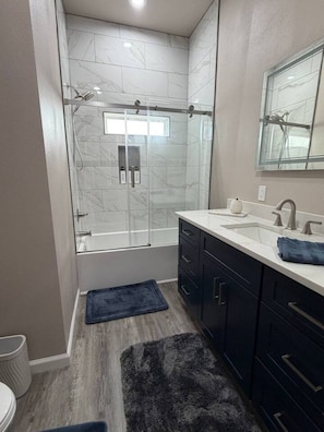 A modern bathroom with a glass-enclosed shower, a white sink with a mirror, and dark cabinets. - Waterfront Retreat | Hot Tub, Outdoor Kitchen & Private Dock (Nocona)