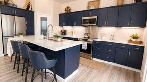 Una cucina moderna con mobili scuri, un'isola centrale con sgabelli da bar, elettrodomestici in acciaio inossidabile e oggetti decorativi sui piani di lavoro.