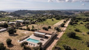 Ein modernes Haus mit Swimmingpool, umgeben von viel Grün und Hügeln.