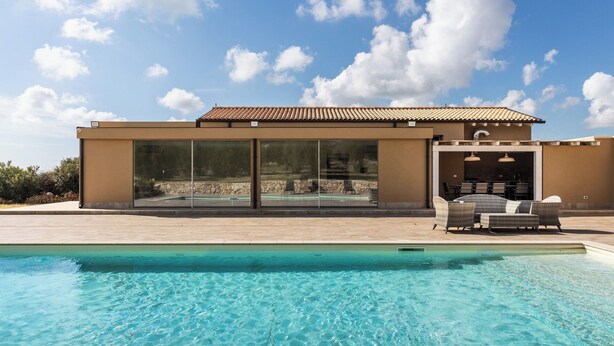 Ein modernes Haus mit Swimmingpool, großen Schiebeglastüren und Gartenmöbeln.