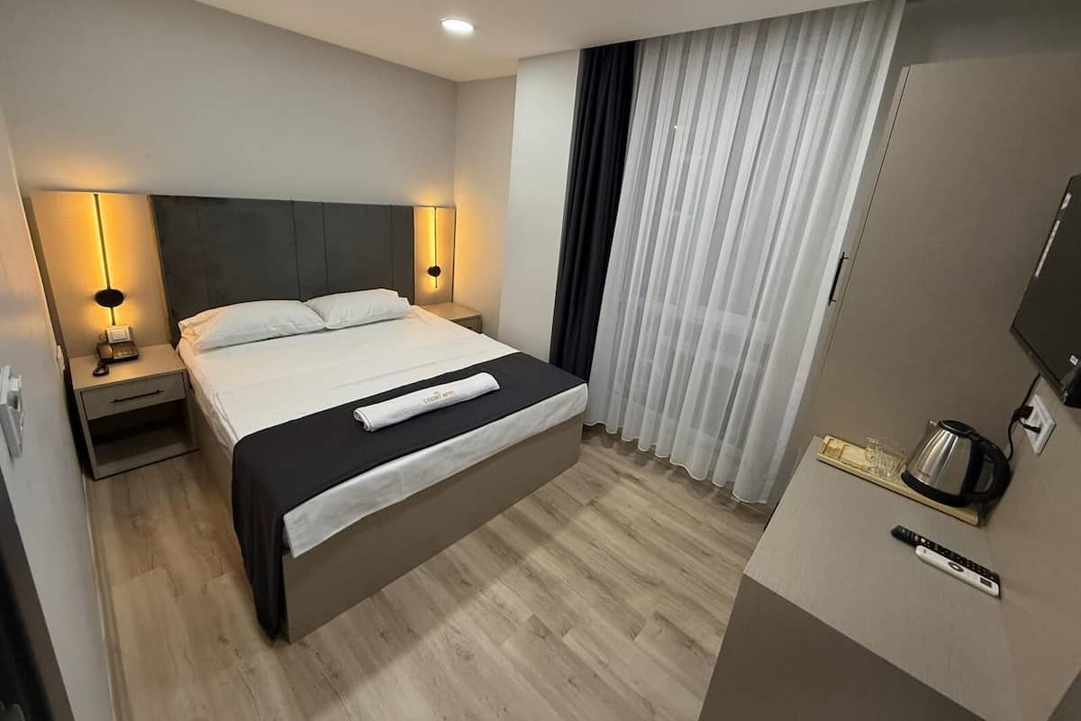 Una habitación de hotel con cama, lámparas de noche, televisión, cafetera y control remoto.