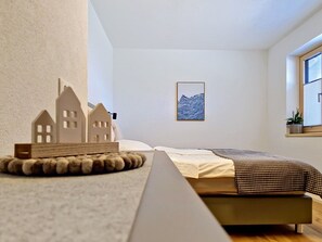Ein Schlafzimmer mit Bett, einem Fenster mit Blick, einem gerahmten Bild an der Wand und einem Modellhaus auf einem Tisch.