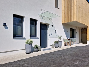 A modern building with a flat facade, large windows, and a wooden deck area with outdoor seating. - Lovely apartment for 6 guests with WIFI, TV and terrace (Kematen In Tirol)