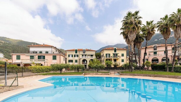 Una piscina circondata da edifici a più piani con balconi, palme e montagne sullo sfondo.