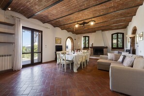 Un salon spacieux avec une cheminée, un coin repas avec une table dressée pour quatre personnes, et un coin salon confortable avec un canapé et des fauteuils.
