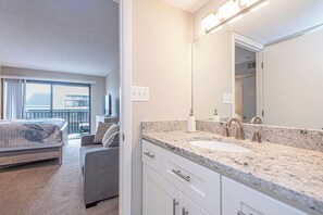 Ein Hotelzimmer mit Bett, Sofa, Badezimmer mit Waschbecken und Spiegel sowie einem Balkon mit Blick.
