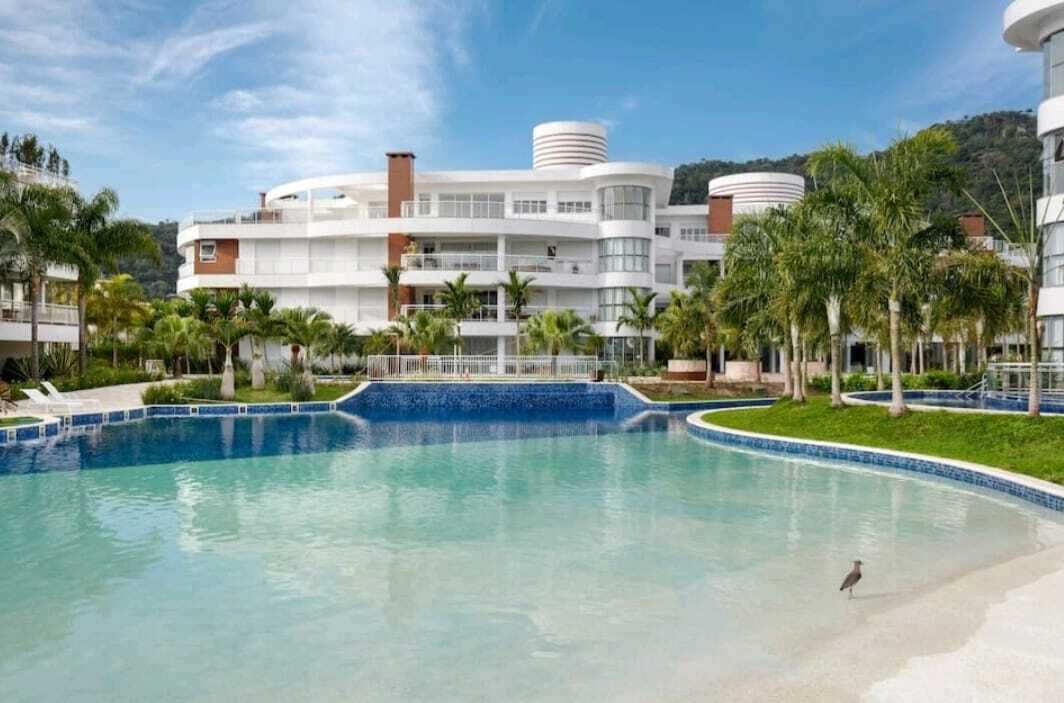 A resort with a large swimming pool, palm trees, and modern buildings with balconies.