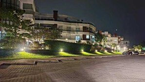 A multi-story building with balconies, a paved road, and parked cars. - Gustavo Funchal (Florianópolis)