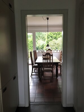 Zona pranzo con tavolo e sedie, un lampadario e vista sul verde circostante.