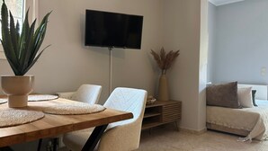 Ett vardagsrum med en platt-TV, ett matbord med underlägg, en soffa och en krukväxt.