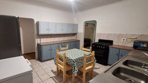 A compact kitchen with a refrigerator, stove, sink, and a table with chairs. - H&L Self-catering Accommodation (Bonnievale)