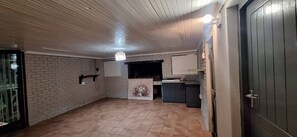 Una habitación con suelo de baldosas, pared de ladrillo, puerta blanca y un pequeño mostrador con un jarrón de flores.