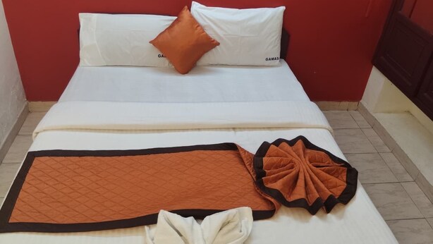 Una cama con ropa de cama blanca, una almohada marrón y una manta marrón.
