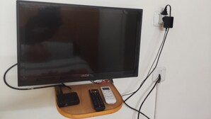 Televisor de pantalla plana sobre un atril de madera, con control remoto y regleta.