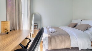 Et hotelværelse med seng, skrivebord, stol, spejl og et vindue med gardiner.