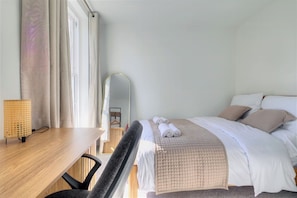 Une chambre d’hôtel avec un lit, un bureau, une chaise, une lampe et un miroir.