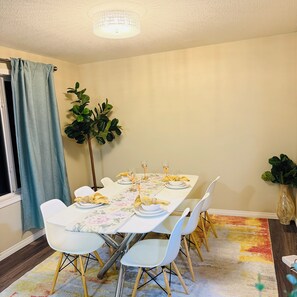 A dining area with a table set for four, white chairs, a floral tablecloth, and a plant in the corner. - Edmonton, Brinell Park, Comfy Guest Retreat, 3BRs 4 Beds + Sofa bed and 2 car GA (Edmonton)