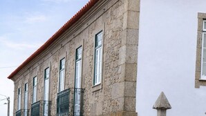 Un edificio de piedra con techo de tejas rojas, varias ventanas y una entrada portonada.