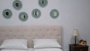 Una cama bien hecha con dos almohadas, una mesita de noche con lámpara y espejos decorativos en la pared.