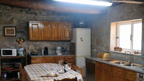 Una cocina rústica con armarios de madera, una mesa de comedor con mantel a cuadros, un refrigerador y una ventana con vistas.