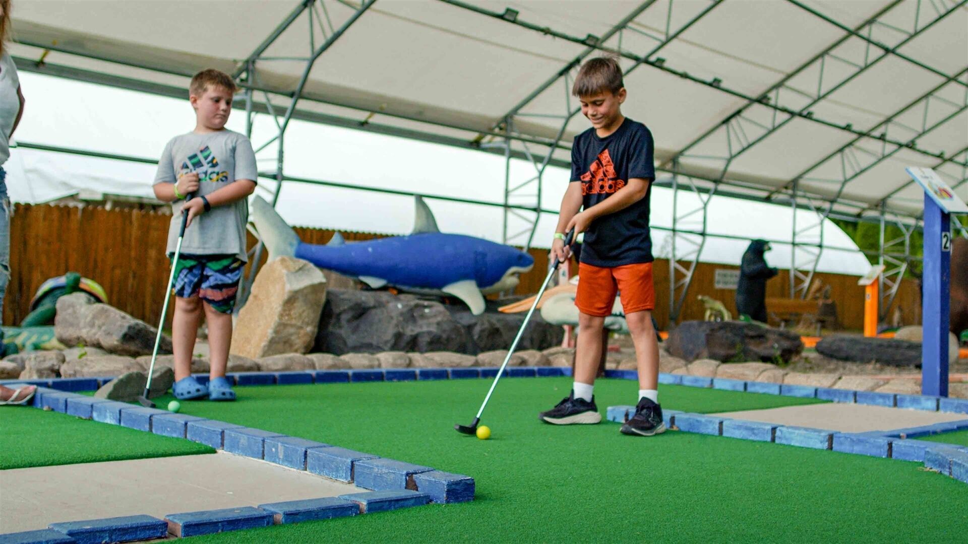 Dos niños jugando minigolf bajo una estructura cubierta.