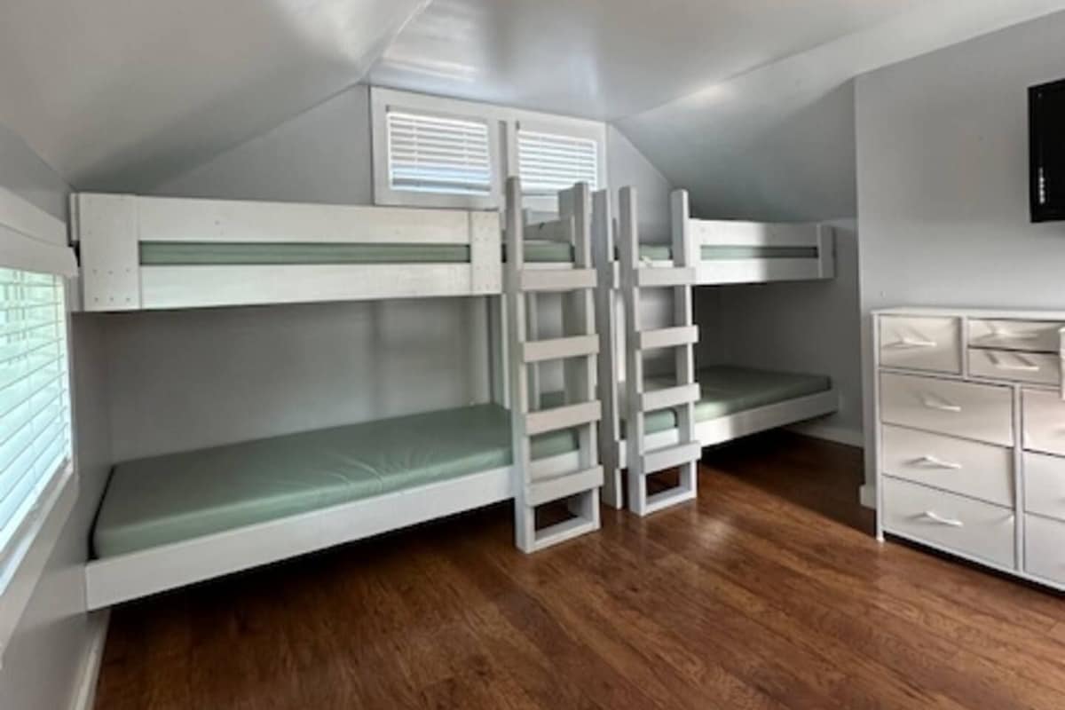 A room with bunk beds, a ladder, a dresser, and a television on the wall.
