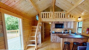 A wooden cabin interior with a kitchen, dining area, and a loft bedroom. - Splash Magic RV Resort (Northumberland)