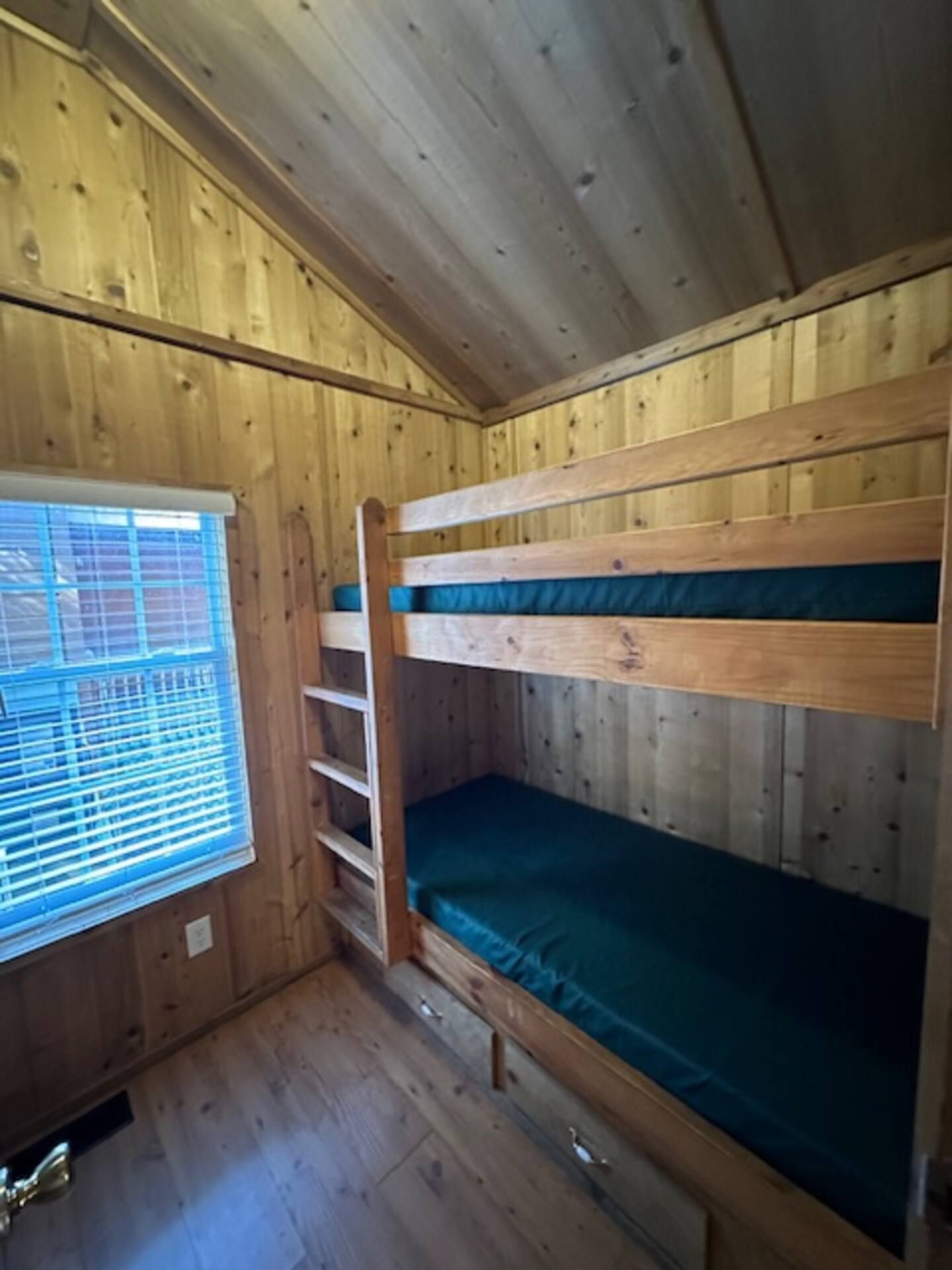Habitación con literas, paredes de madera y ventana con persianas.