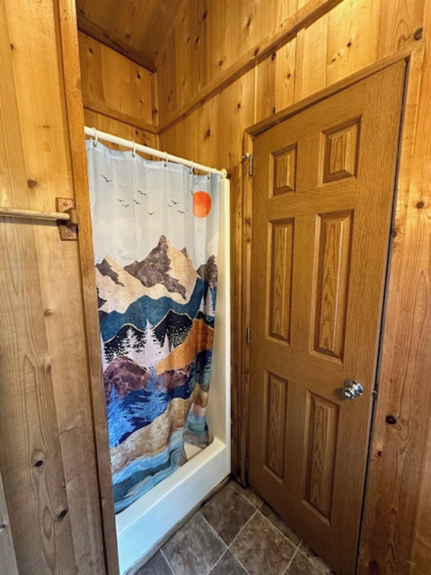 A wooden interior with a shower curtain featuring a mountain and bird design, a wooden door, and tiled flooring.
