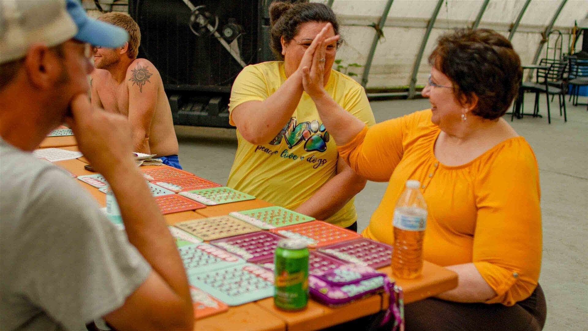A group of people seated at a table with playing cards and a can of soda.