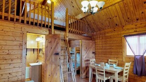 A wooden cabin interior with a dining area, a staircase, and a bathroom. - Splash Magic RV Resort (Northumberland)
