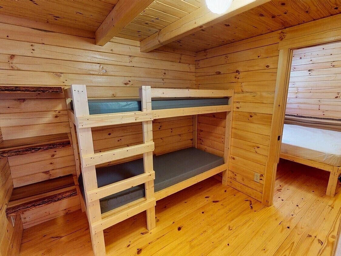 Ein Holzblockhaus im Inneren mit Etagenbetten, Holzboden und geneigter Decke.