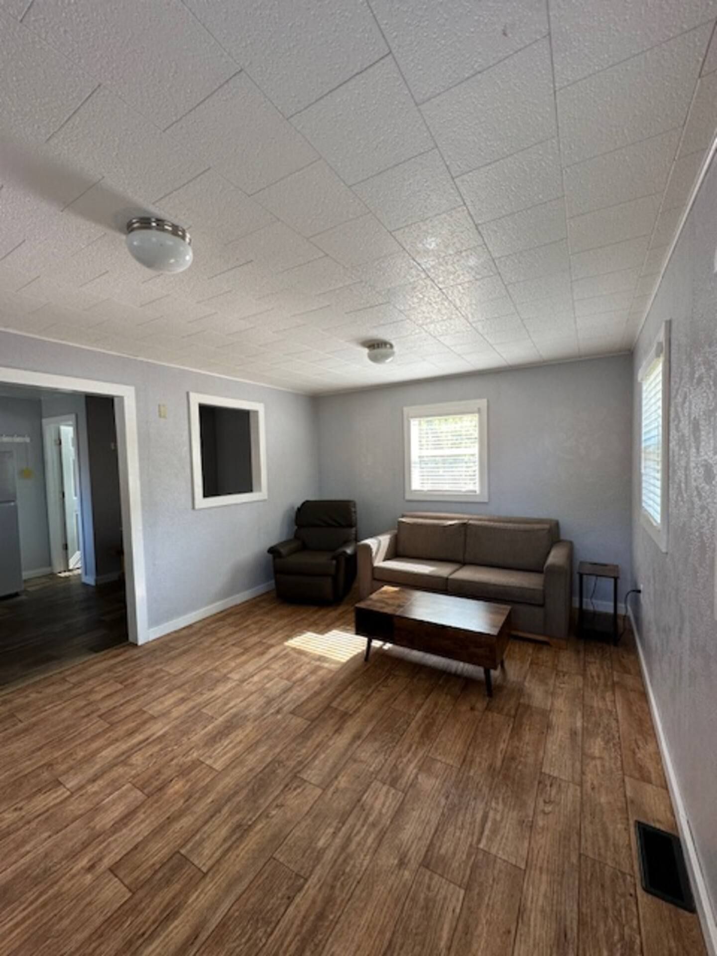 A spacious living room with a wooden floor, a sofa, a chair, and a coffee table.