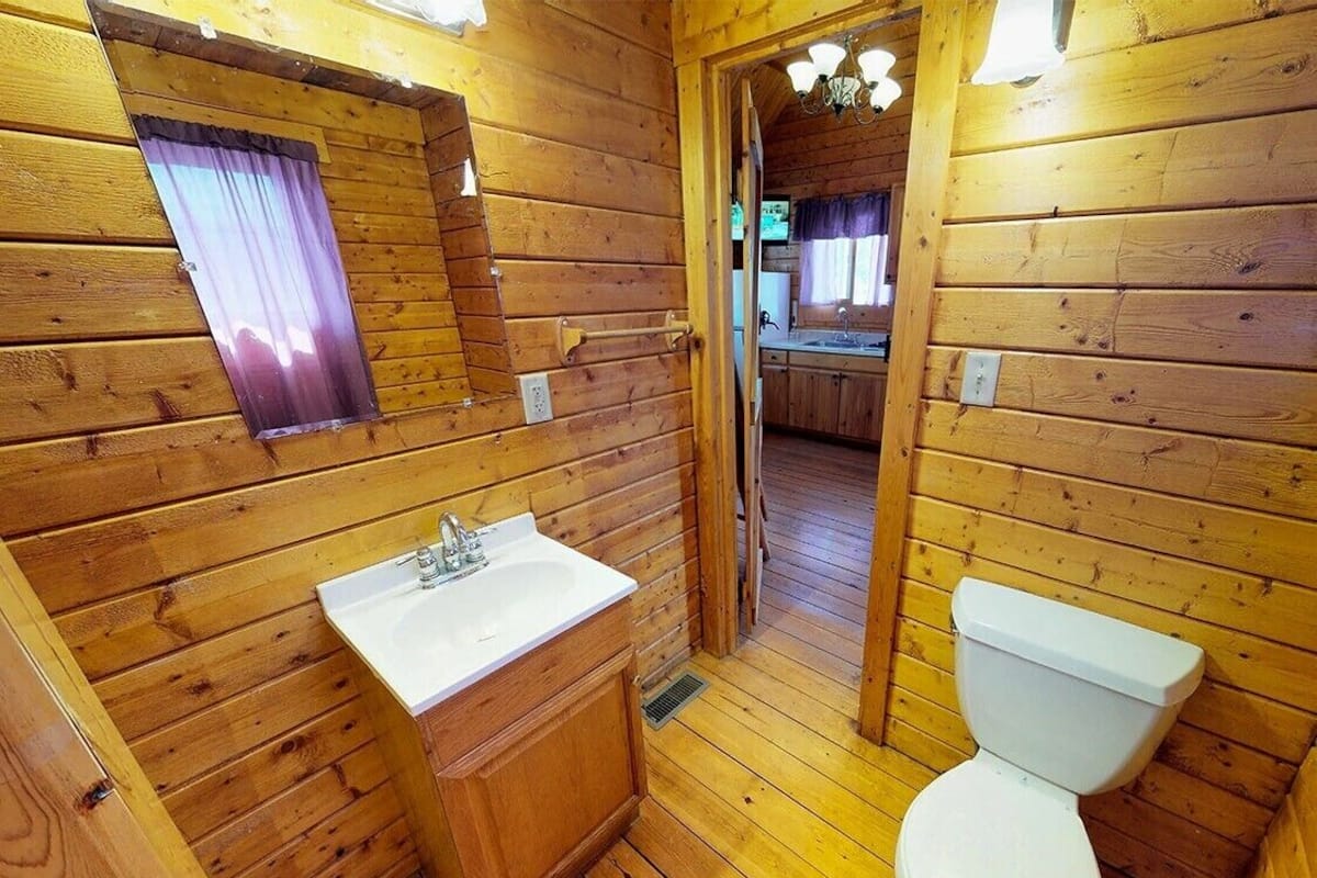 A wooden cabin bathroom with a sink, toilet, and a window with a curtain.
