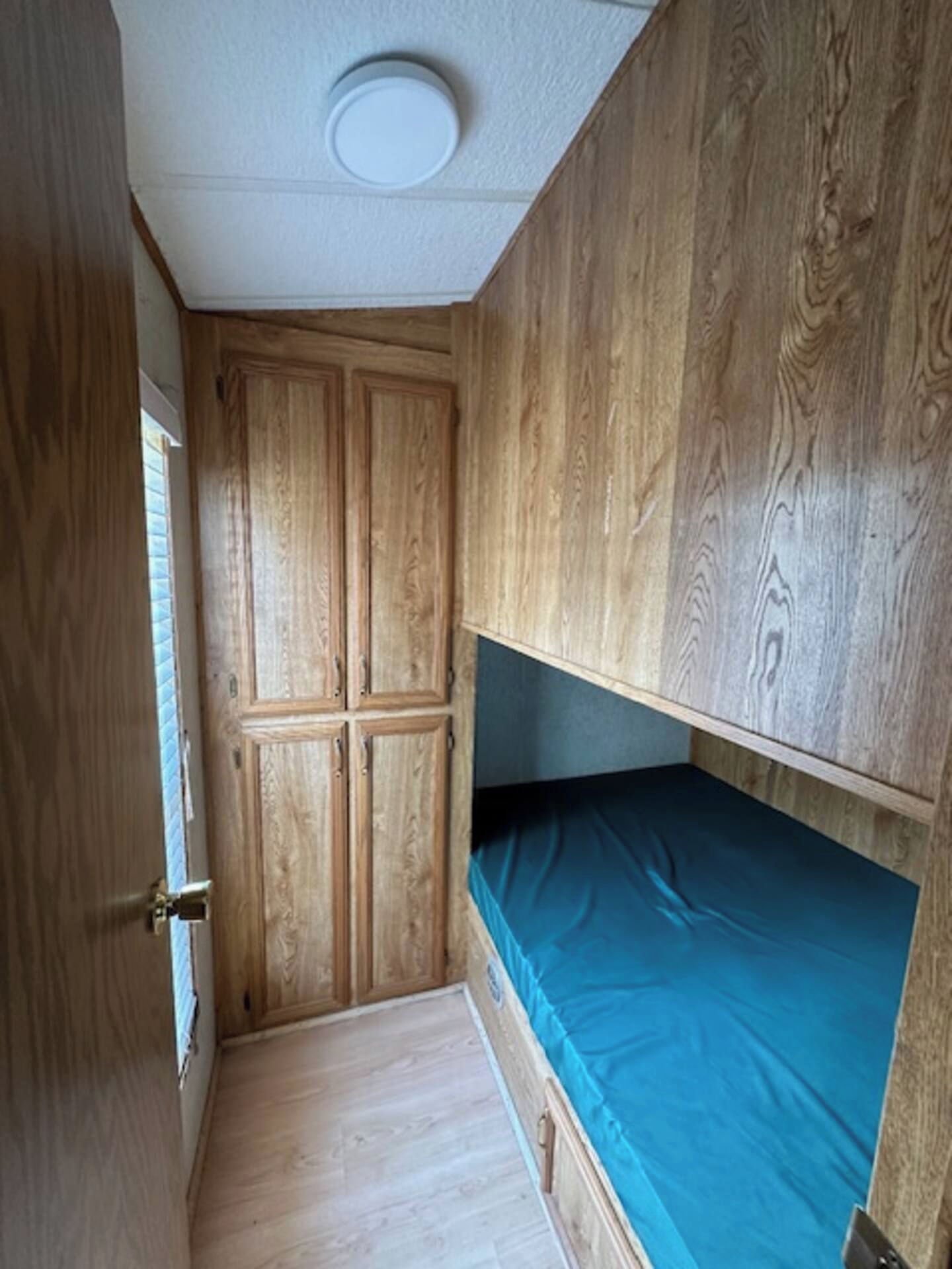 Habitación pequeña con literas, armario de madera y una puerta estrecha.