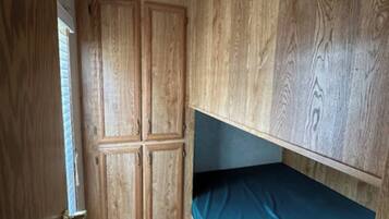 Habitación pequeña con literas, armario de madera y una puerta estrecha.