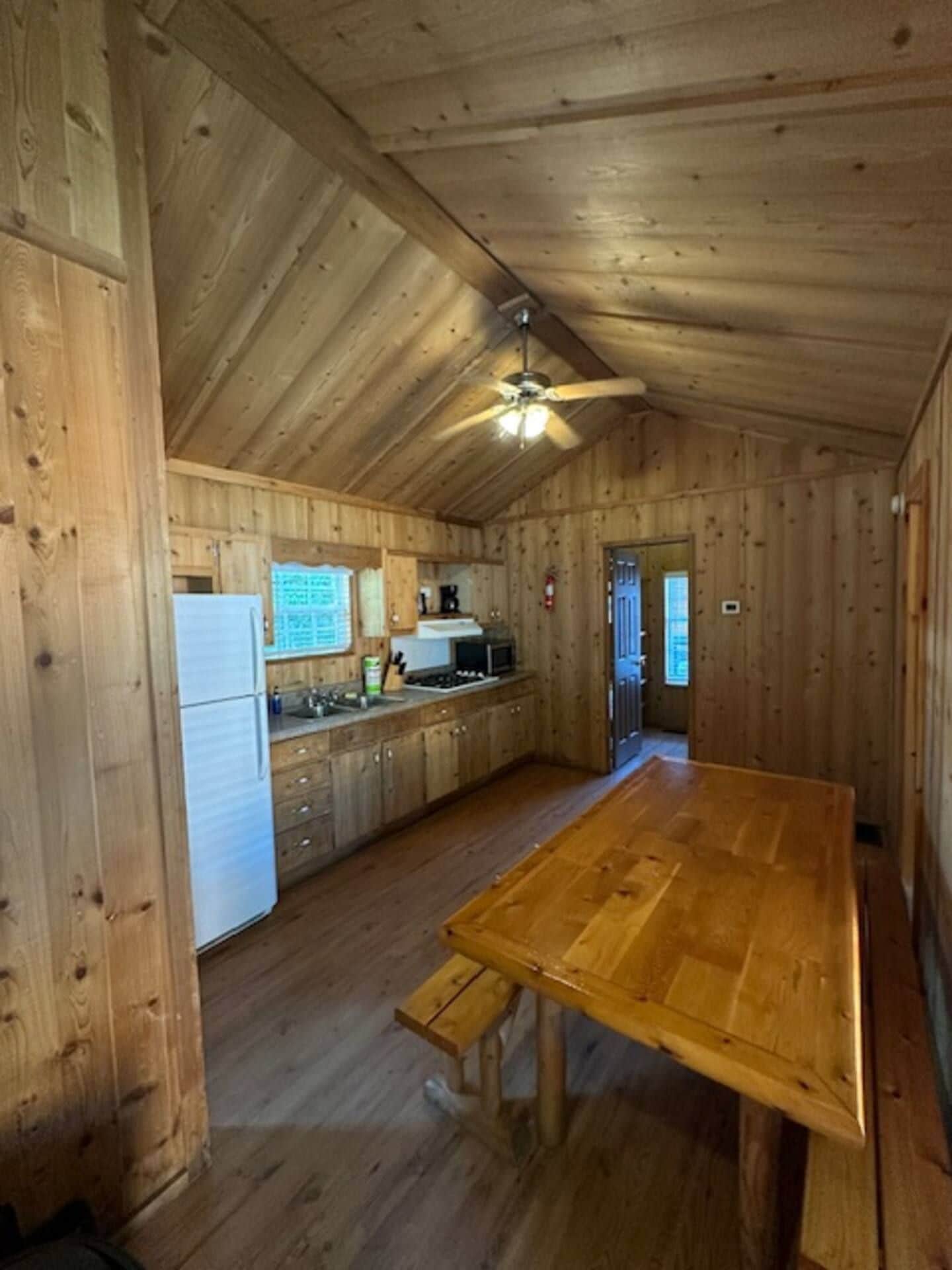 A wooden interior with a kitchen area, a dining table, and a ceiling fan.