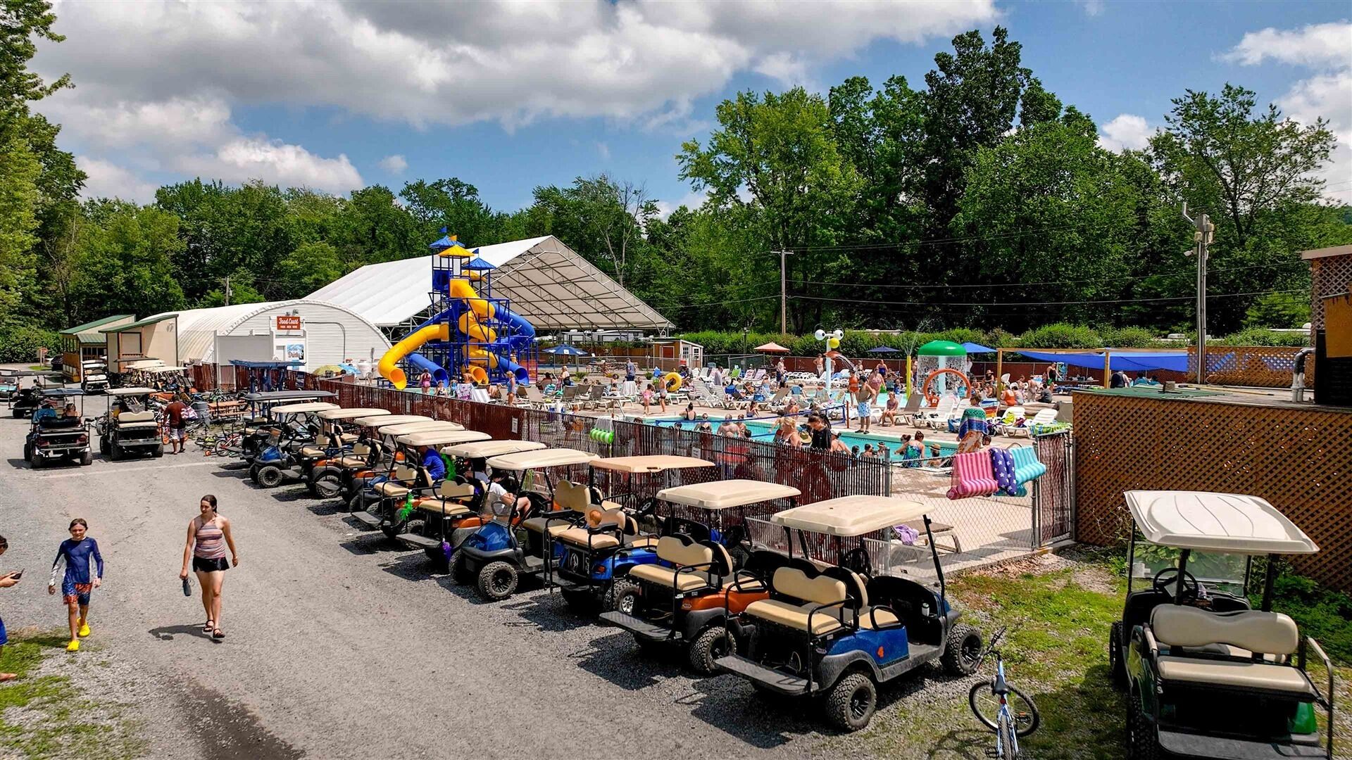 A parking lot with golf carts lined up, a water park with slides, and a crowd of people.