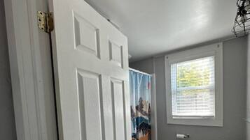 A bathroom with a white door, a window with blinds, a sink, and a shower curtain.