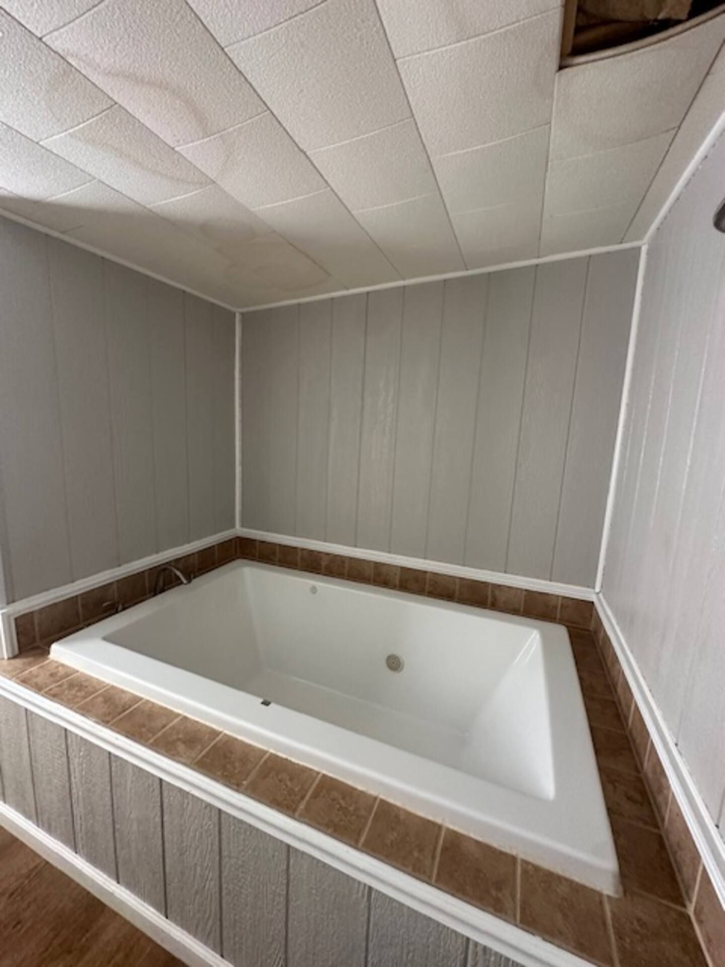 A rectangular bathtub with a white interior and brown tiles at the base, set against a wall with vertical paneling.